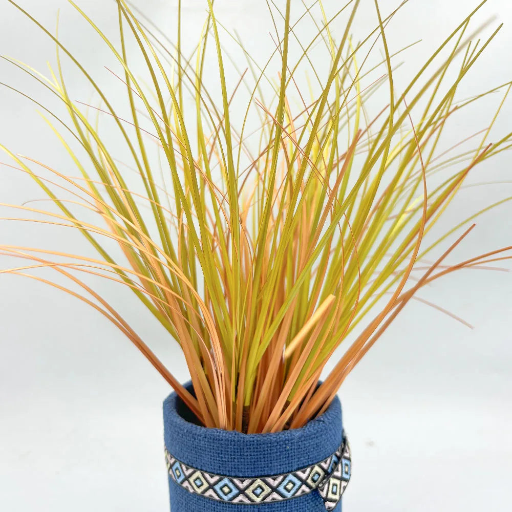 A bundle of artificial grass greenery with golden and reddish-brown blades planted in a blue pot.