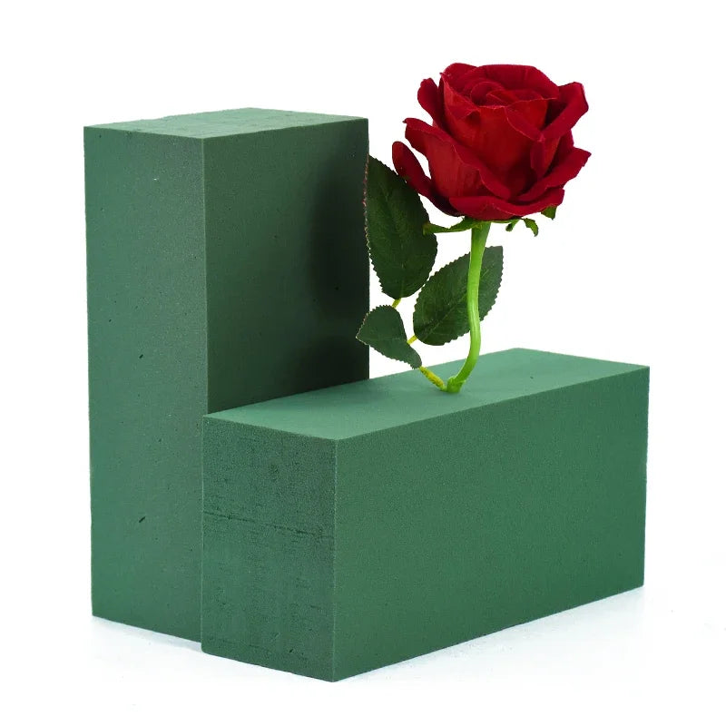 A vibrant red rose is placed on a green foam block, with another block visible beside it.