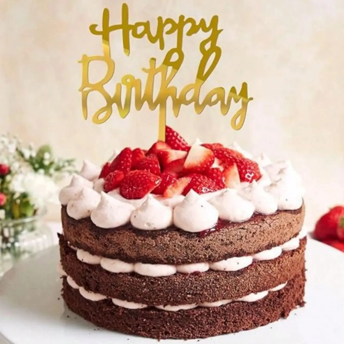 A stack of dark chocolate birthday cake layers topped with fresh strawberries and a gold acrylic happy birthday topper.