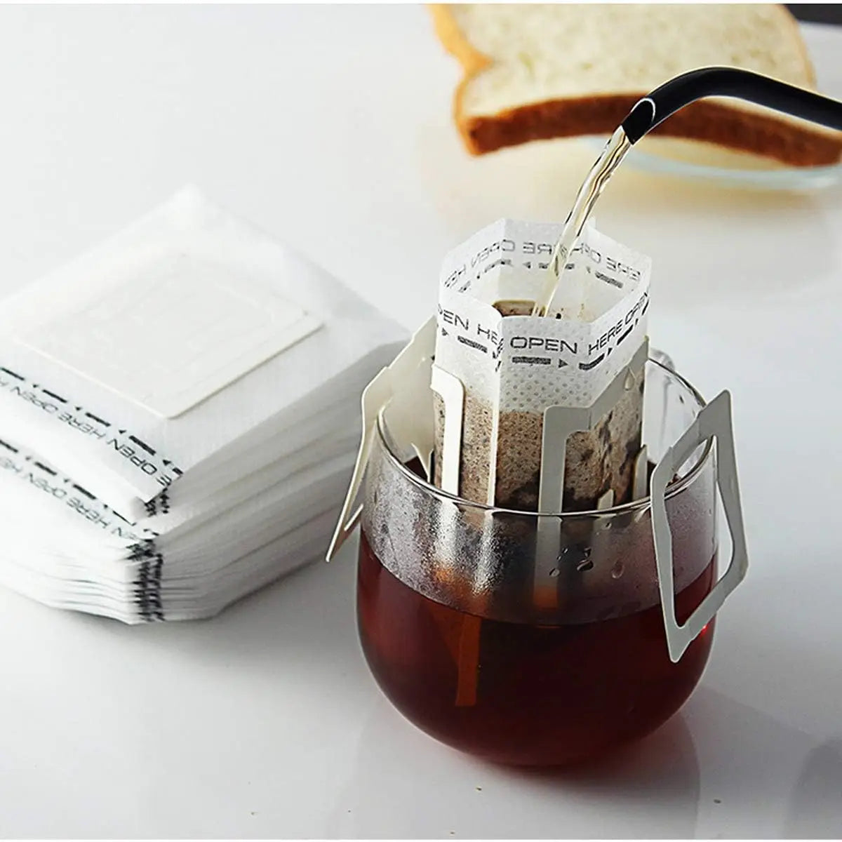 A black coffee filter bag is being filled with brewed coffee in a glass, next to a stack of white disposable filters.