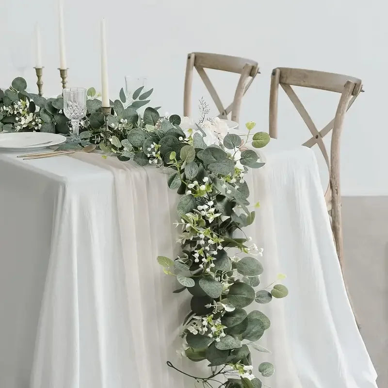 Guirlande d'eucalyptus artificielle drapée sur une nappe blanche pour décoration de mariage ou de maison.