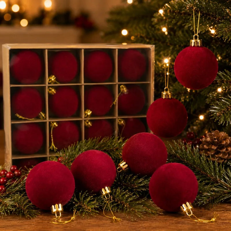 A close-up of velvet red flocked Christmas ball ornaments displayed on a wooden surface surrounded by pine greenery.