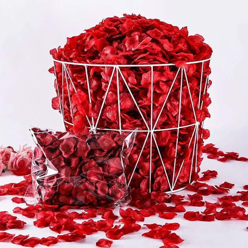 A large cylindrical container filled with bright red artificial rose petals, with some scattered on a white surface.