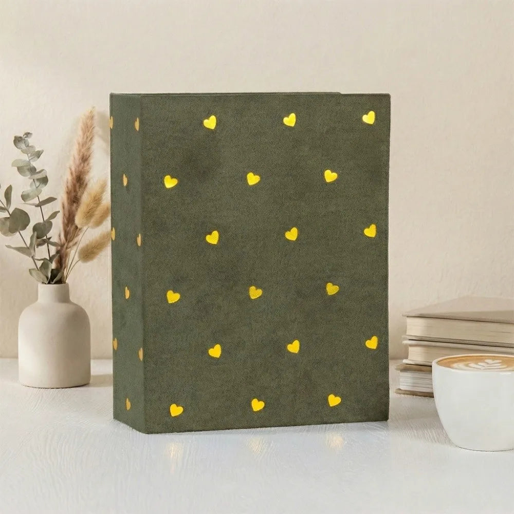 A dark olive green laminated photo album with gold heart patterns resting on a white surface.