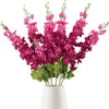 Un bouquet de fleurs artificielles de delphinium roses et magenta dans un vase blanc.