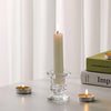 A tall white candle in a glass holder sits on a gray surface next to a small candle.