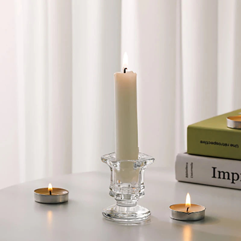 A tall white candle in a glass holder sits on a gray surface next to a small candle.