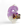 A purple glitter number six candle decorated with small character figures.