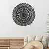 Decoración de pared mandala de metal negro sobre una superficie de madera con un sombrero de paja.