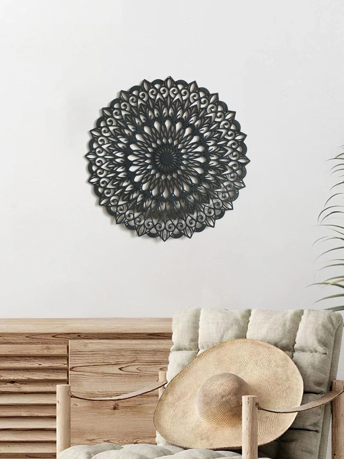 Decoración de pared mandala de metal negro sobre una superficie de madera con un sombrero de paja.