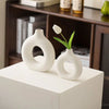 White ceramic vase shaped like a donut holding a single white tulip flower