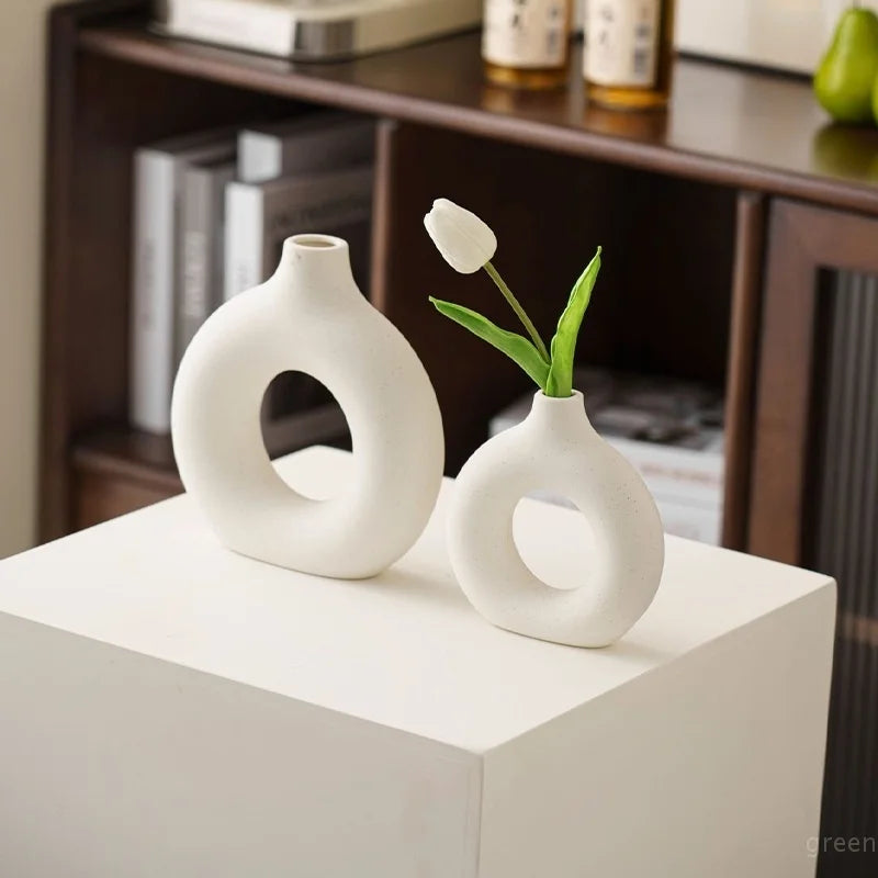 White ceramic vase shaped like a donut holding a single white tulip flower