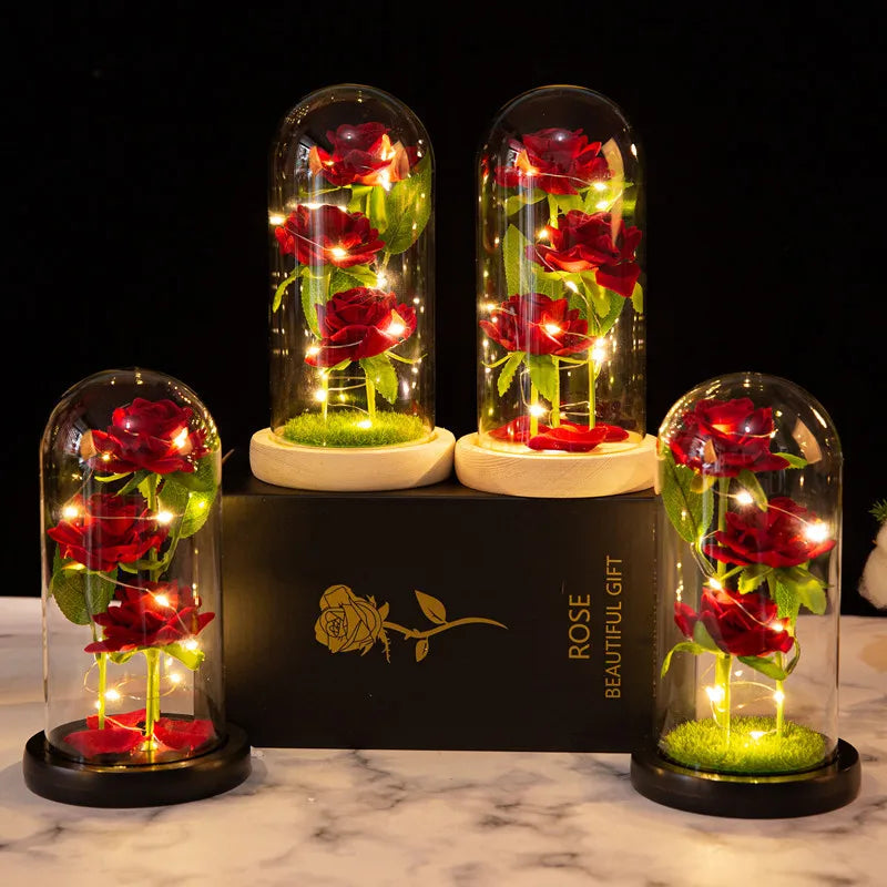 Three glass domes display artificial red roses illuminated by LED lights on a black box.