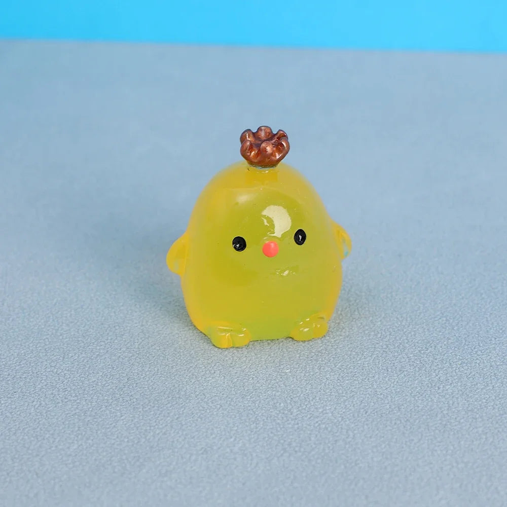 A small, yellow resin chicken ornament with a brown comb and black eyes resting on a gray surface.
