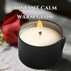 A black candle in a dark holder with a warm glow, set against a red rose.