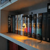 A row of vintage books is displayed on a shelf illuminated by a black metal lantern lamp.