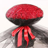 A bouquet of red silk roses wrapped in black sheer fabric with a bright red ribbon.