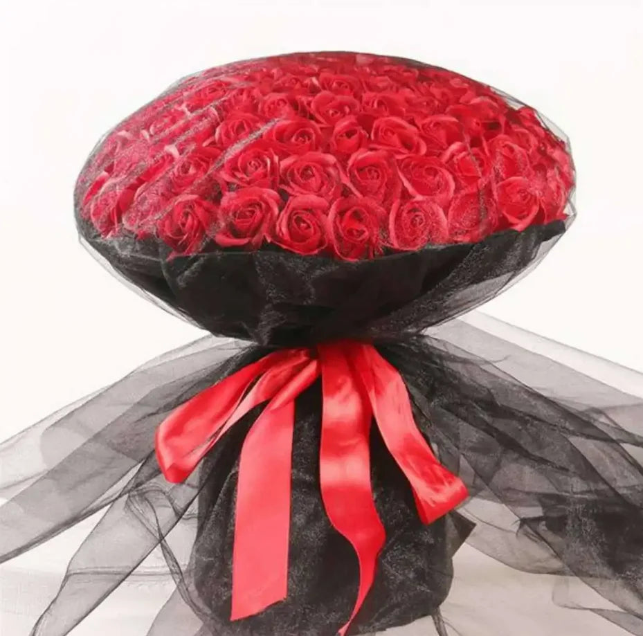 A bouquet of red silk roses wrapped in black sheer fabric with a bright red ribbon.