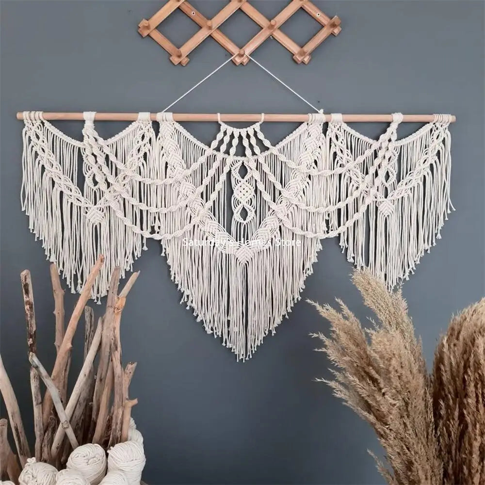 Handwoven boho macrame wall hanging tapestry with white fringe suspended on a wooden rod against a gray wall.