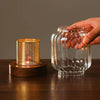 A hand holds a vintage wooden candle lantern with a glass cover, illuminating a glowing candle inside.