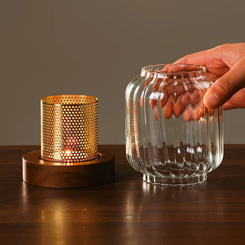 A hand holds a vintage wooden candle lantern with a glass cover, illuminating a glowing candle inside.
