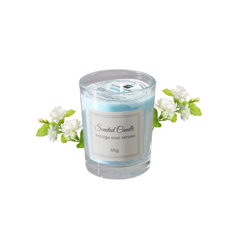 A clear glass jar of scented candle with a light blue wax and white flowers.