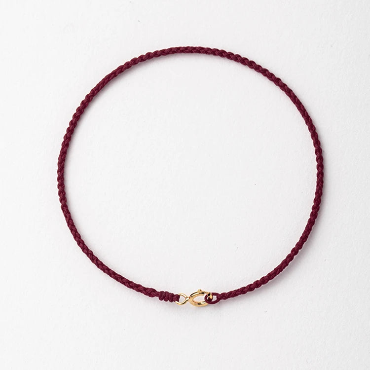 A handmade red string bracelet with a gold plated clasp, shown against a white background.