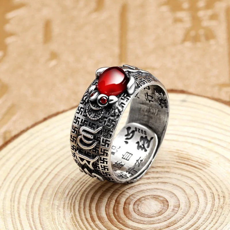 Silver ring with a red gemstone and coin details resting on a wooden surface.