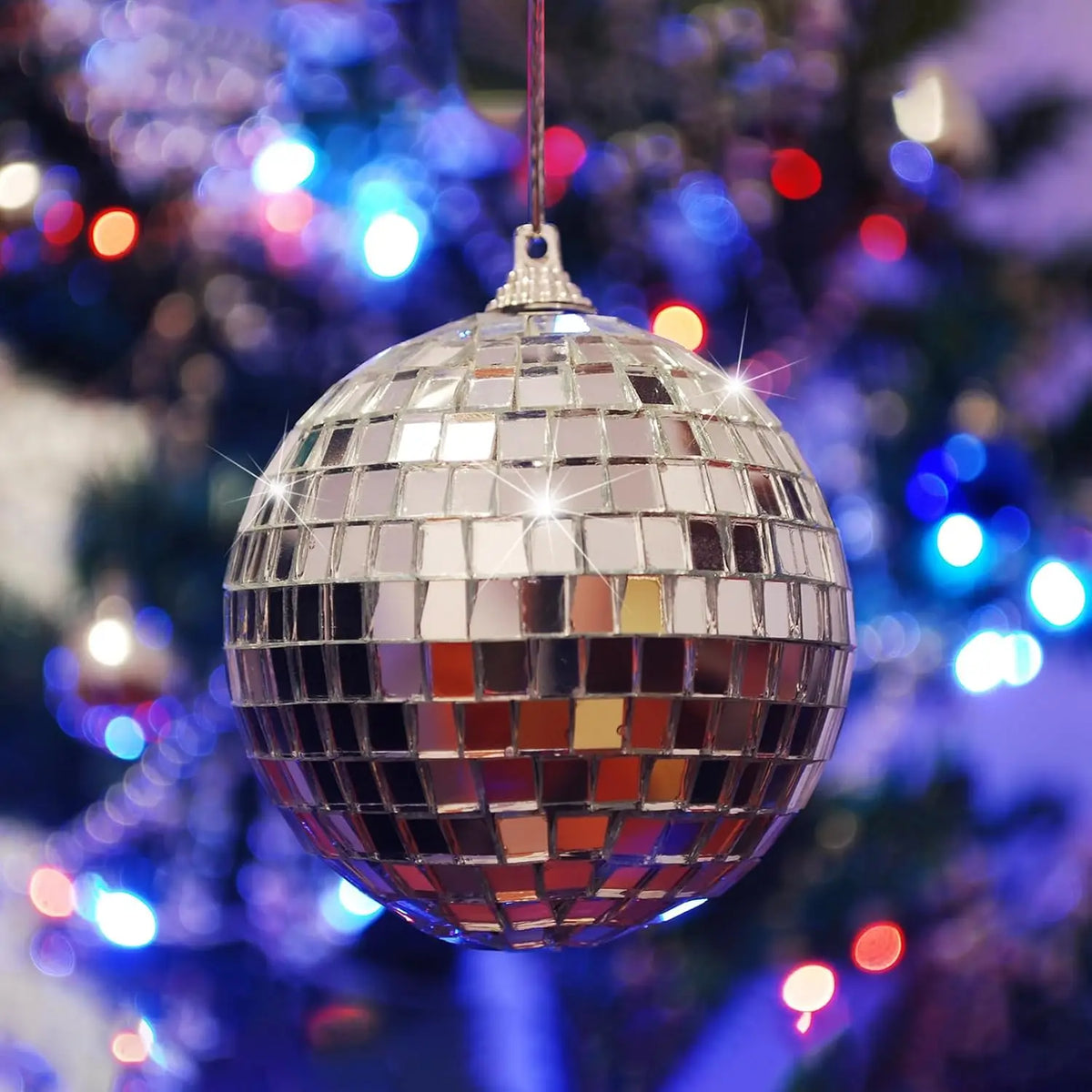 A silver, spherical mirror ball ornament hanging on a Christmas tree decorated with blue lights.