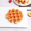 A golden waffle is displayed on a white plate, with a single red berry visible in the background.