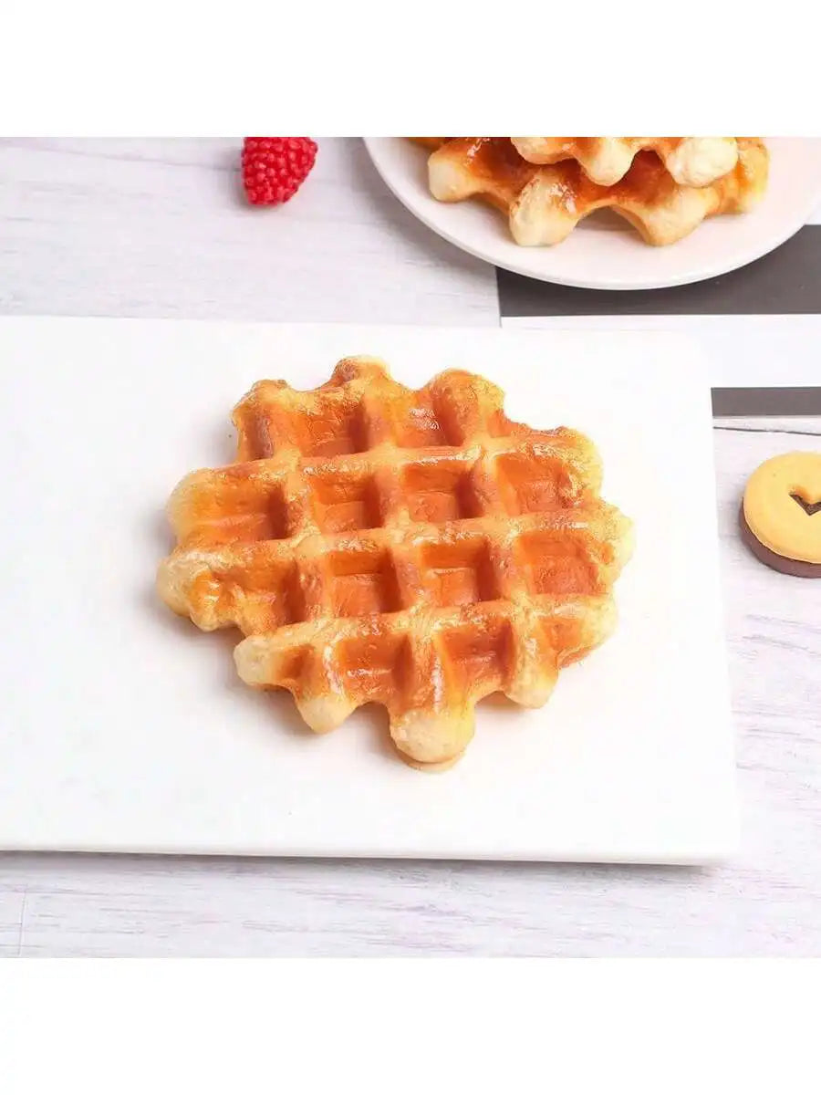 A golden waffle is displayed on a white plate, with a single red berry visible in the background.