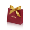 A red paperboard thank you gift bag tied with a gold ribbon, featuring the word Merci printed on it.