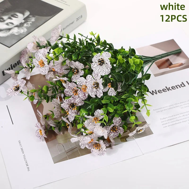 White artificial daisy flower bundles with green foliage displayed on a piece of paper.