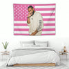 Un homme en chemise claire devant un mur décoratif d'une tapisserie avec un drapeau américain rayé rose et blanc.