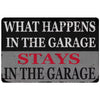 A distressed metal tin sign with white text on a dark background that reads What happens in the garage stays in the garage