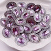 A pile of purple and pink gemstone flatback rhinestones for crafting arranged on a white surface.