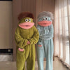 A pair of fuzzy green and blue monster onesie pajamas for couples standing in a room.