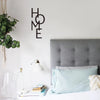A bedroom scene featuring a metal word art sign spelling HOME above a bed with light blue pillows and a modern lamp.