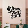 A black metal sign with the text Welcome to Our Home mounted on a light pink wall.