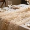 Sheer beige pearl gauze fabric draped across a white table setting with beaded trim.
