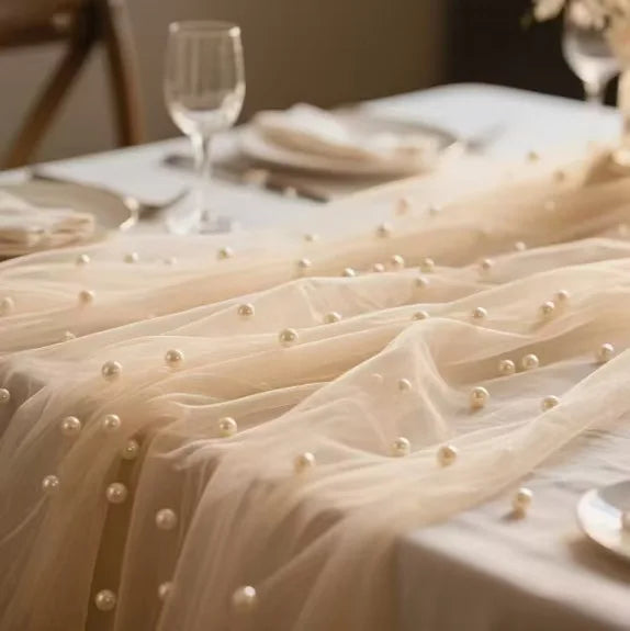 Sheer beige pearl gauze fabric draped across a white table setting with beaded trim.