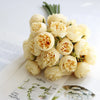 A bouquet of artificial pink peony silk flowers with green stems displayed on white paper.