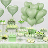 A display of light green heart-shaped foil balloons and various green desserts on a white table.