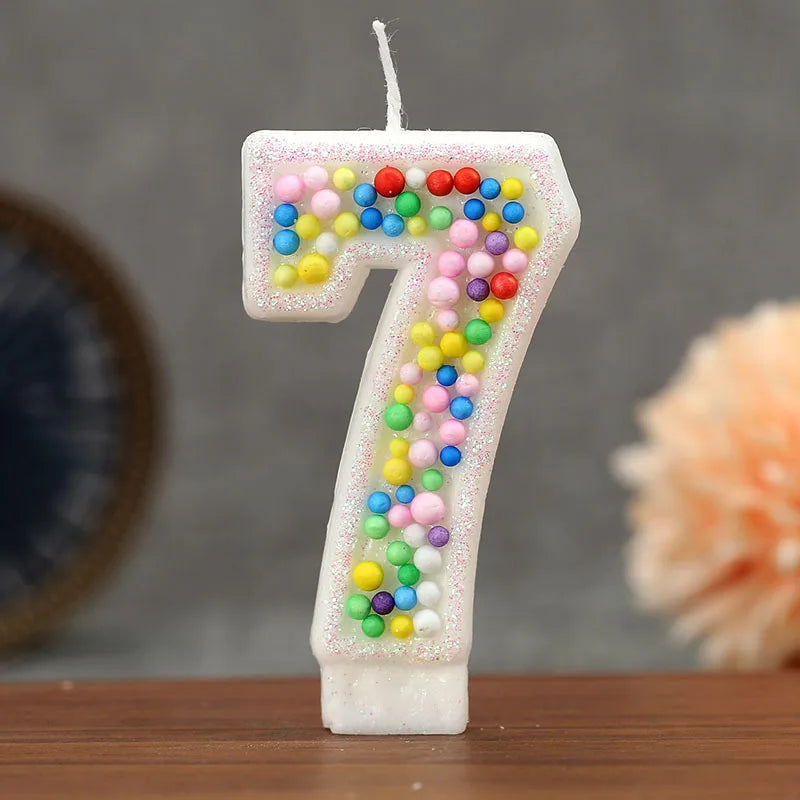 A white birthday candle shaped like the number seven decorated with colorful candy beads
