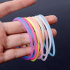 A hand holds a set of ten glow-in-the-dark silicone bracelets in various pastel colors.