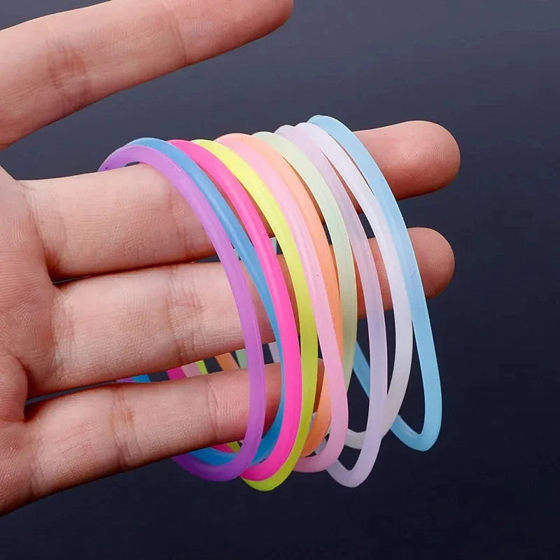 A hand holds a set of ten glow-in-the-dark silicone bracelets in various pastel colors.