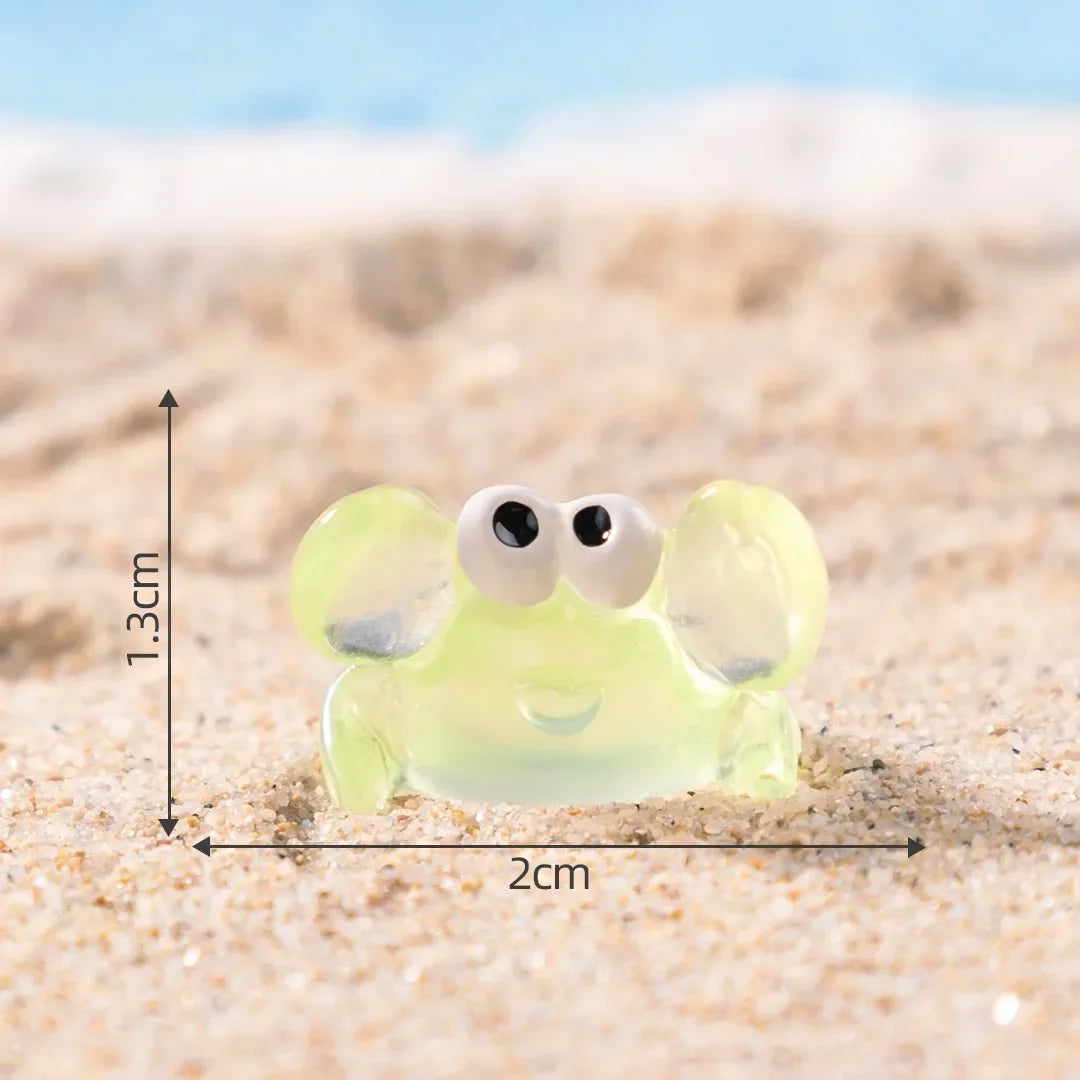 A small, translucent yellow resin crab decor with large eyes resting on a sandy beach.