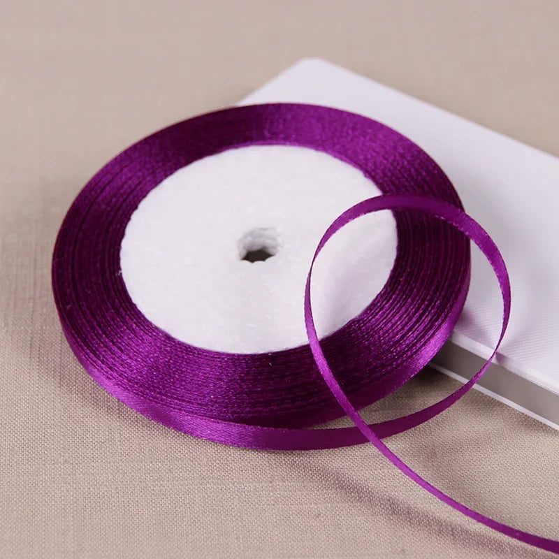 A purple satin ribbon spool is shown on a white card against a beige background.
