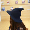 A dark navy vintage knit witch hat worn by a person against a light wood background.