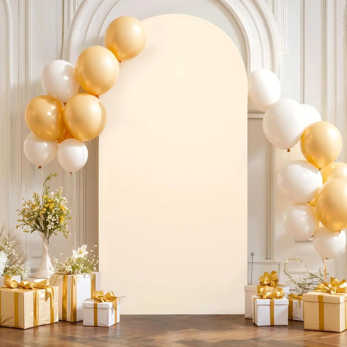 A cream-colored arch backdrop decorated with gold and white balloons and floral arrangements.